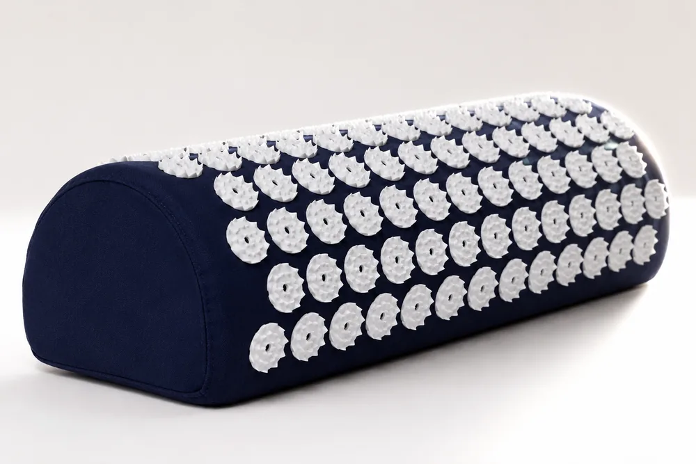 Close side view of the navy SpikeRest bolster pillow covered in white spike disks
