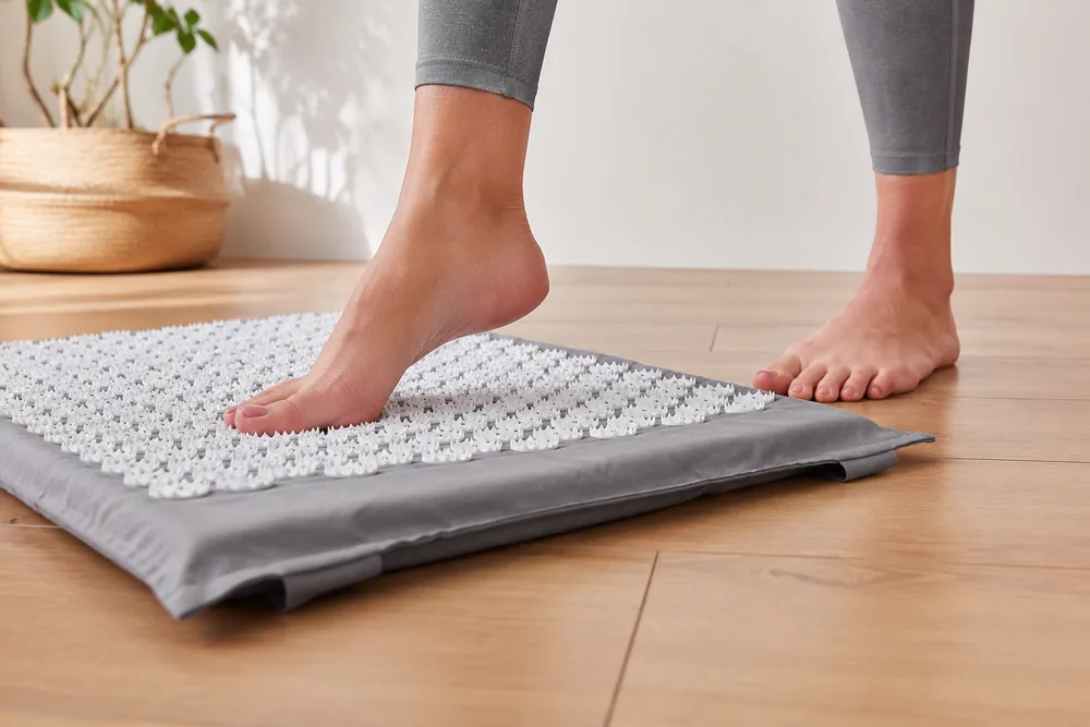 One bare foot stepping onto a gray SpikeRest acupressure mat while the other stays on the floor