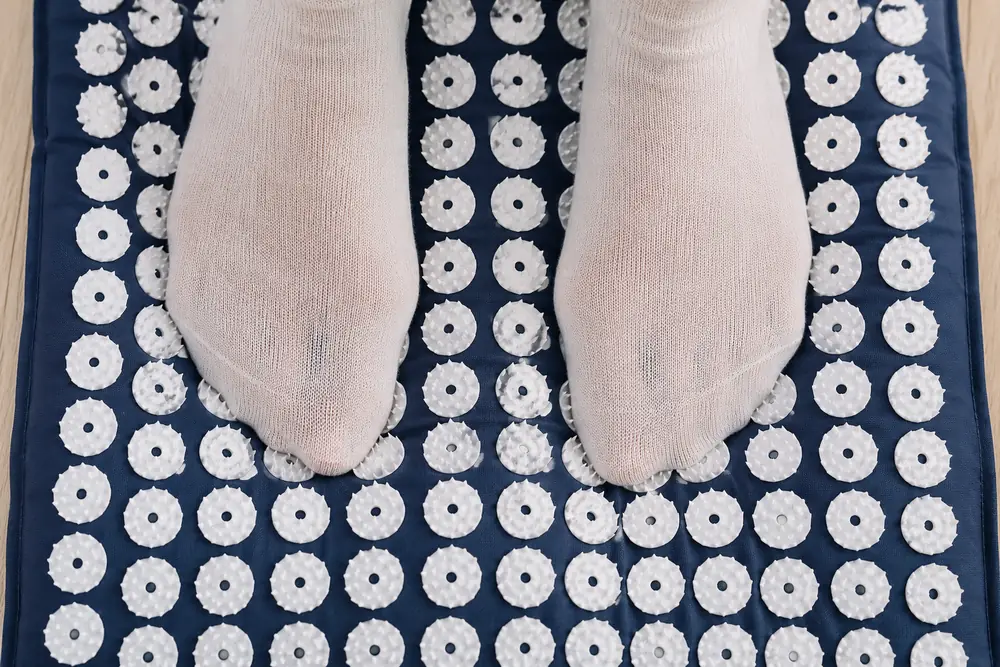 Feet in thin cotton socks resting on a navy SpikeRest acupressure mat, the fabric slightly tented by the white spike disks