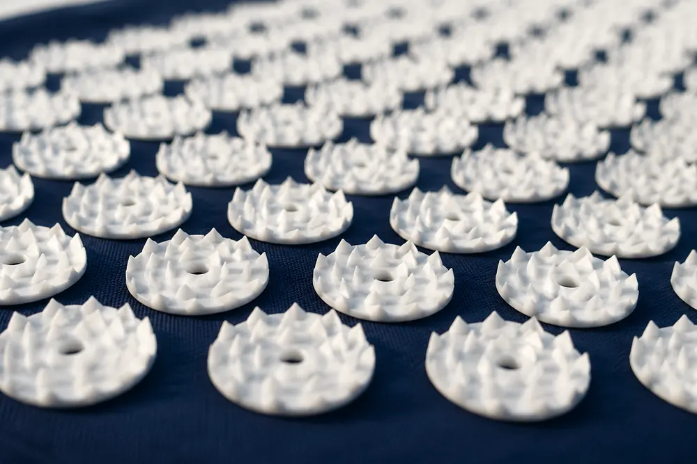 Close view of the white spike disks on a navy SpikeRest mat seen at a low angle, rows receding into soft focus