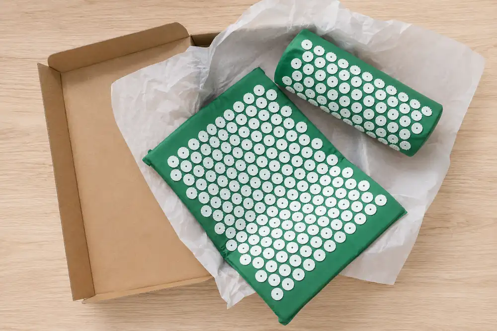 Green SpikeRest mat and bolster pillow lifted from a plain kraft box with tissue paper on a light wood table